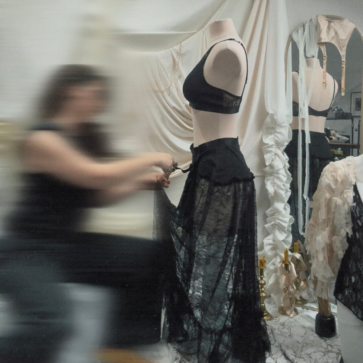 Person adjusting a black lace garment on a mannequin in a store setting.